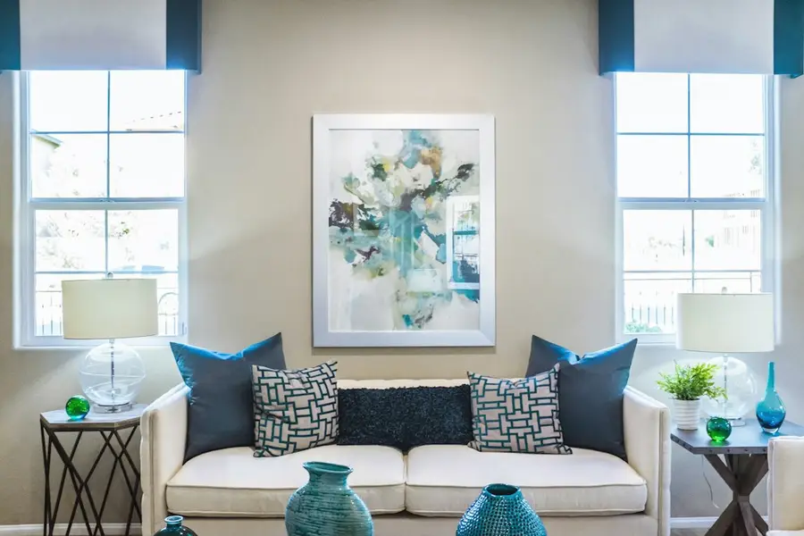 A quiet sitting room with a cream sofa, two windows, and a small plant in soft daylight